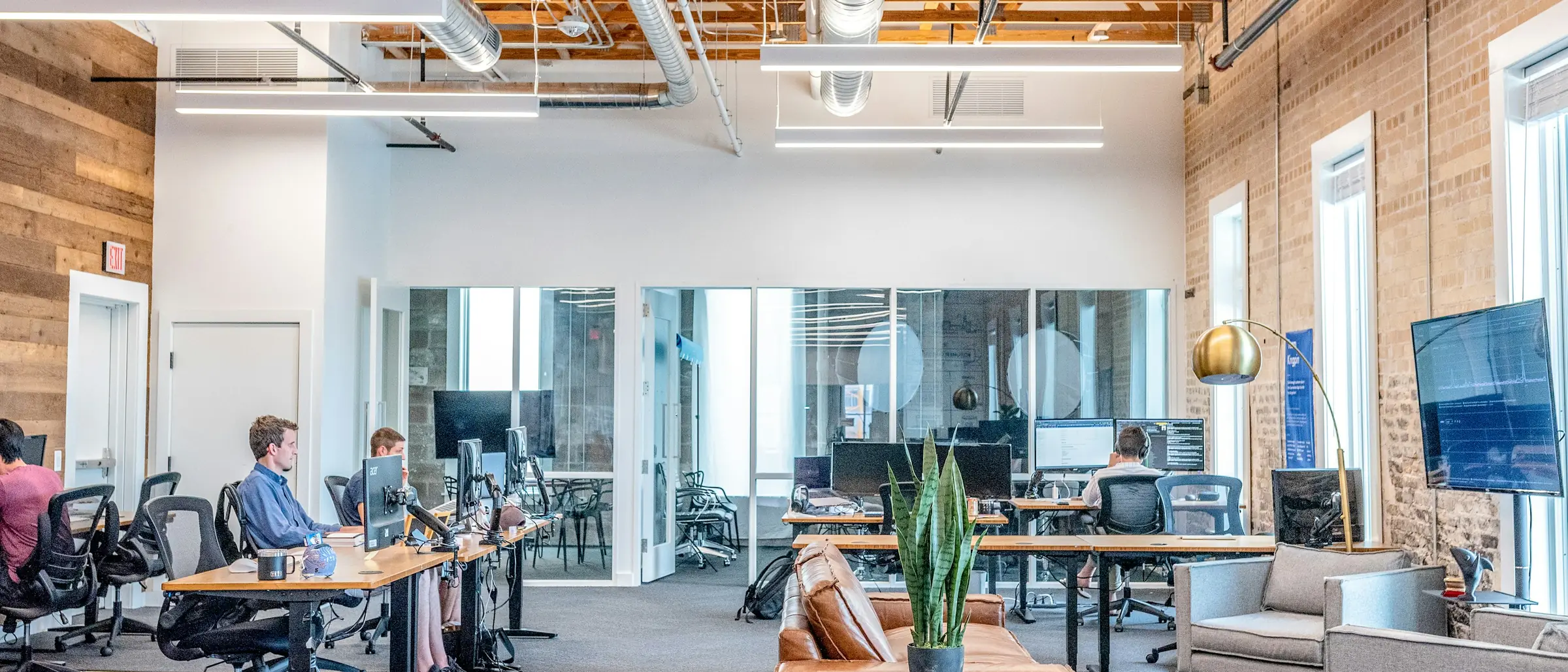 Bright open-plan office with desks, monitors and glass-walled meeting rooms