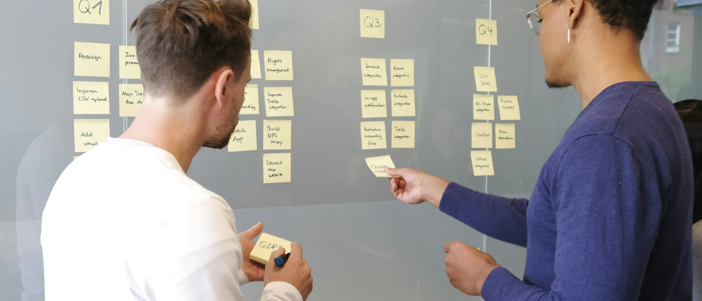 Two engineers planning work with sticky notes on a glass wall