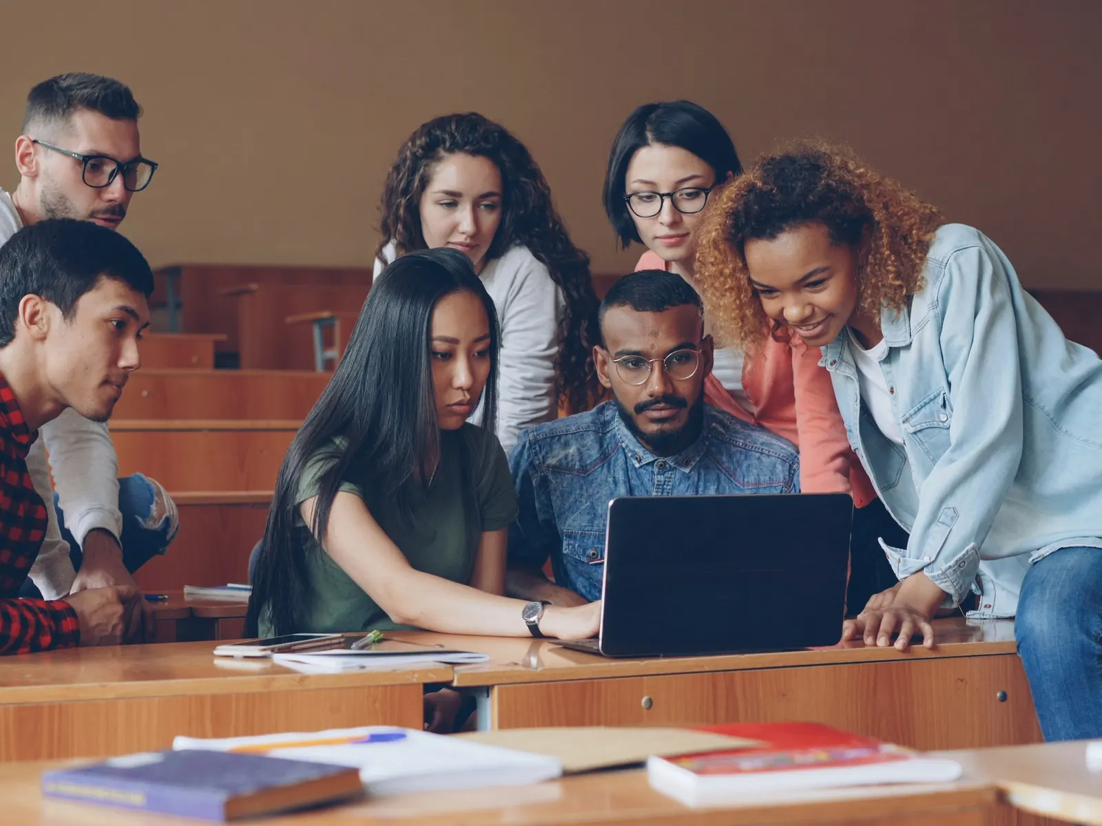 Students gathered around a laptop in a university lecture hall